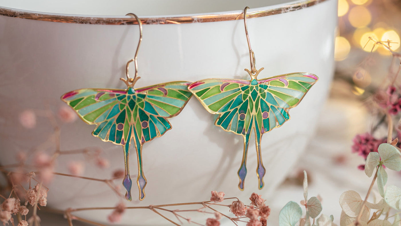 Luna moth earrings on a white cup with floral background