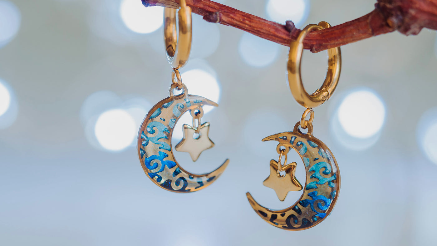 Gold earrings with moon and star designs hanging on a branch against a blurred light background